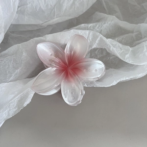 Détail d'une pince à cheveux fleur rose dégradé avec une finition mate sur tissu blanc