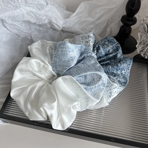 Détail d'un chouchou en satin bleu dégradé avec texture mouchetée sur plateau verre