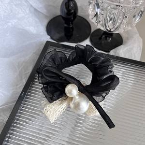 Détail d'un chouchou en maille noire avec bordure en dentelle beige et perles