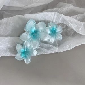 Détail macro de la pince à cheveux fleur de frangipanier avec dégradé bleu nacré