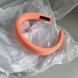 Detail showing coral orange fabric headband with a black handmade woven label on inner side