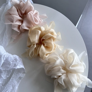 Close-up of three large organza scrunchies in pink, champagne gold, and cream white