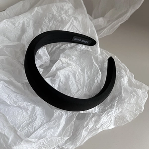 Detail of a padded black satin headband featuring a handmade woven label on a white background