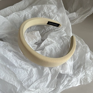 Detail of beige wide padded headband featuring a woven handmade label on white paper