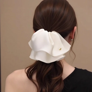 Detail of white satin ruffle hair clip with gold metal accent on model's hair