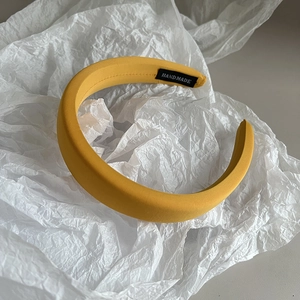 Detail of yellow fabric headband featuring a black handmade label on pleated paper