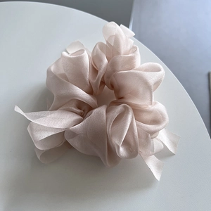 Detail of light champagne organza scrunchie with soft pleated texture on white surface