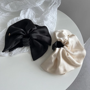 Detail view of large satin bow hair claws in black and cream with a silky finish