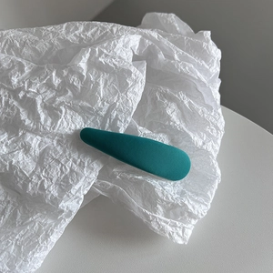 Gros plan d'une barrette à cheveux en tissu bleu cyan sur un fond de papier minimaliste