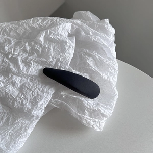 Gros plan sur une pince à cheveux BB en tissu mat noir sur fond de papier blanc texturé