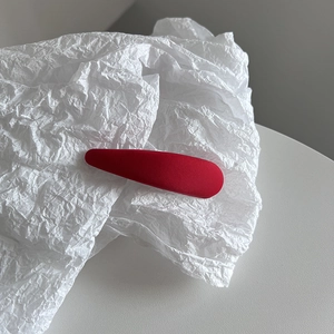 Détail d'une pince à cheveux rouge en tissu sergé sur un fond blanc texturé élégant