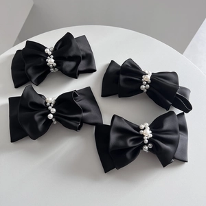 Elegant black satin double-layered bow hair clips with pearls on a white surface