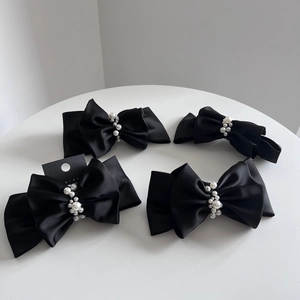 Detail of four black satin double bow hair clips with white pearl accents on white table