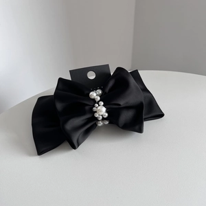 Detail of elegant black satin bow hair clip featuring polished white pearls on fabric