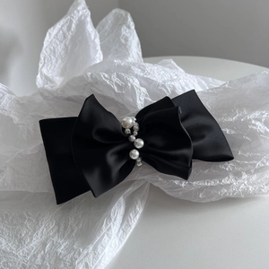 Detailed macro of a black satin double-layered bow hair clip featuring elegant white pearls