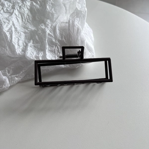 Detailed view of a sleek black rectangular hair claw clip with a hollow metal frame design