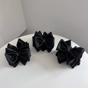 Lot de trois pinces à cheveux avec nœuds noirs et strass sur un socle blanc rond