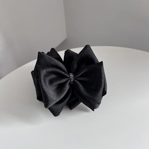 Détail d'une pince à cheveux à nœud noir avec paillettes argentées et strass élégants