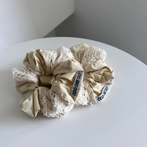 Detail of cotton beige scrunchie with white lace embroidery and ODD ONE OUT label