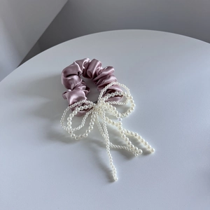 Detail van een roze satijnen scrunchie met elegante parelstrik en lange kwastjes