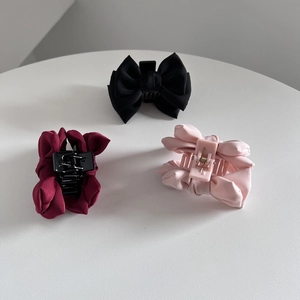 Three elegant satin bow hair claws in black, burgundy and pink on a white pedestal