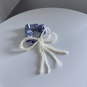 Detailopname van de paarse satijnen scrunchie met elegante witte parel-strikkwastjes