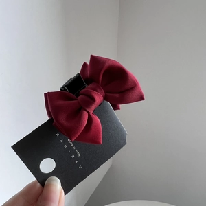 Detailed macro view of a dark red fabric ribbon bow hair clip with black brand tag