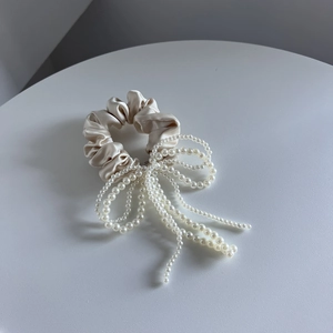 Detail van elegante satijnen scrunchie met parelmoeren strik in champagnegoud