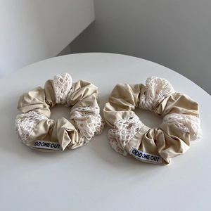Detailed close-up of beige cotton and white lace embroidery scrunchie with brand label