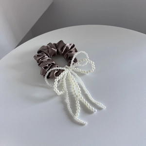 Detail van elegante bruine satijnen scrunchie met witte parelmoer en hangende kwastjes