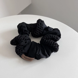 Detailed view of black cotton scrunchie with lace patchwork and brand woven label