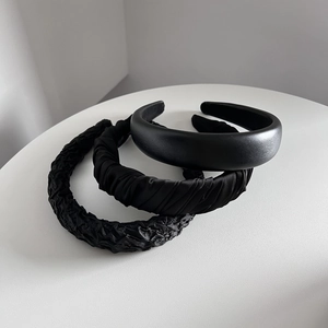 Trois serre-têtes noirs texturés : lisse, plissé et gaufré, présentés sur un socle blanc