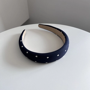 Dettaglio del cerchietto in denim blu navy con cuori bianchi su un piedistallo bianco