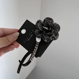 Close-up of elegant black rhinestone camellia hair clip with silver metal charm