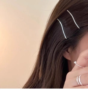 Close-up of wavy silver hair clips and minimalist rings on a model with brown hair