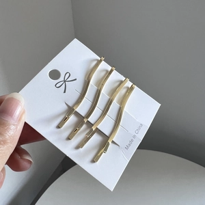 Detail of four golden wavy minimalist hair clips on white card packaging