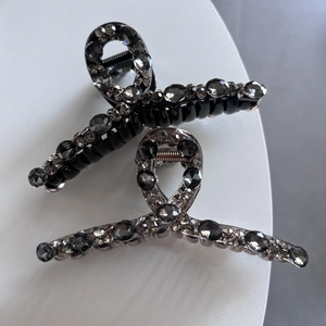 Dettaglio di pinze per capelli di lusso con strass grigi su sfondo grigio minimalista