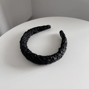 Détail d'un serre-tête noir plissé avec texture en similicuir sur support blanc