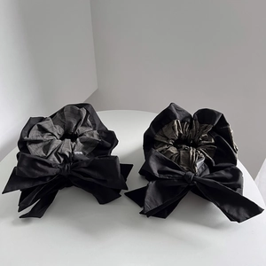 Detail of grey and green striped scrunchies with large black bows on a white surface