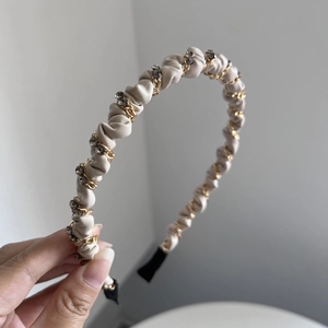 Close-up of beige pleated leather headband with gold metal chain and dark grey rhinestones