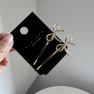 Pair of gold metal bow hair clips on black display card held by hand showing the design