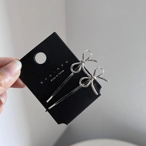 Close-up of silver metal bow hair clips on a black card showing fine linear texture