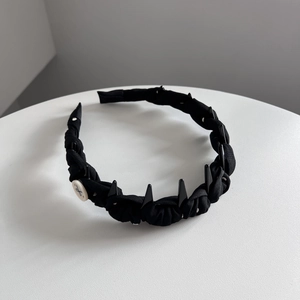 Détail d'un serre-tête en tissu plissé noir avec peigne intérieur et bouton latéral