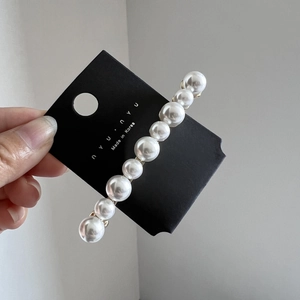 Gros plan d'une barrette élégante avec dix perles blanches brillantes sur carte d'affichage