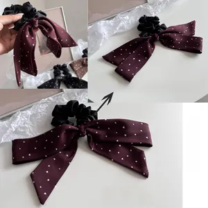 Detail of a black scrunchie with wine red satin bow featuring tiny white heart patterns
