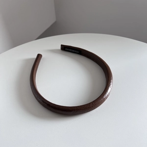 Détail d'un serre-tête en cuir marron avec une étiquette en tissu noir fait à la main
