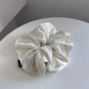 Detail of white satin scrunchie featuring camellia embroidery and Hand Made label