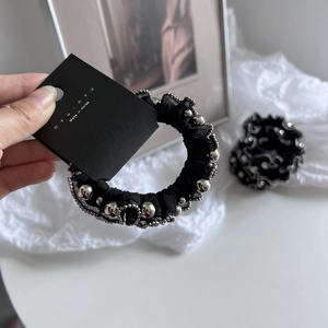 Classic black scrunchie with silver bead detailing and nyunyu brand tag on lace background