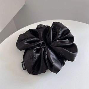 Close-up of black satin scrunchie featuring 3D rose embossing and a Hand Made label
