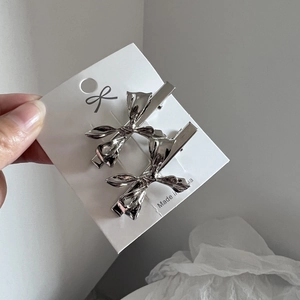 Paar minimalistische silberne Haarklammern mit Schleifen-Design auf einer Displaykarte